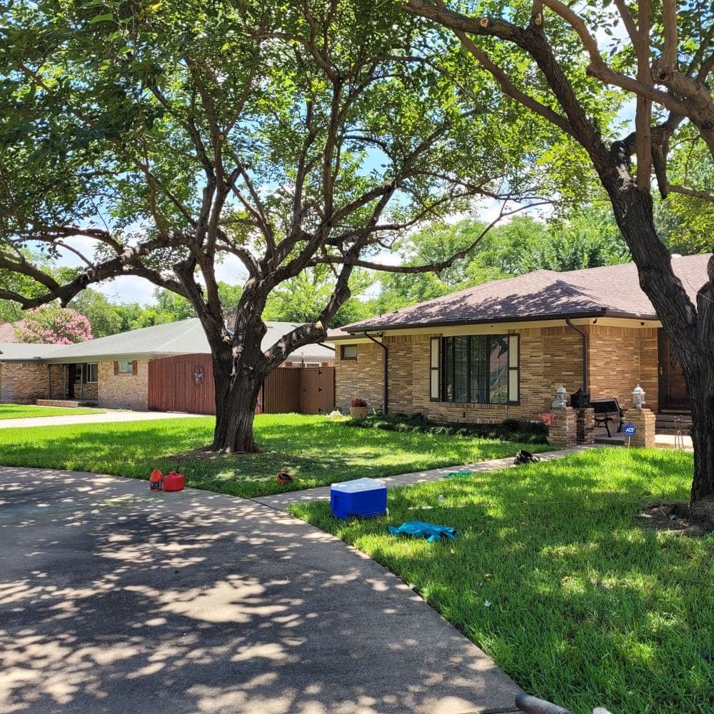 Charming suburban home with lush green lawn and large shade trees on a sunny day.