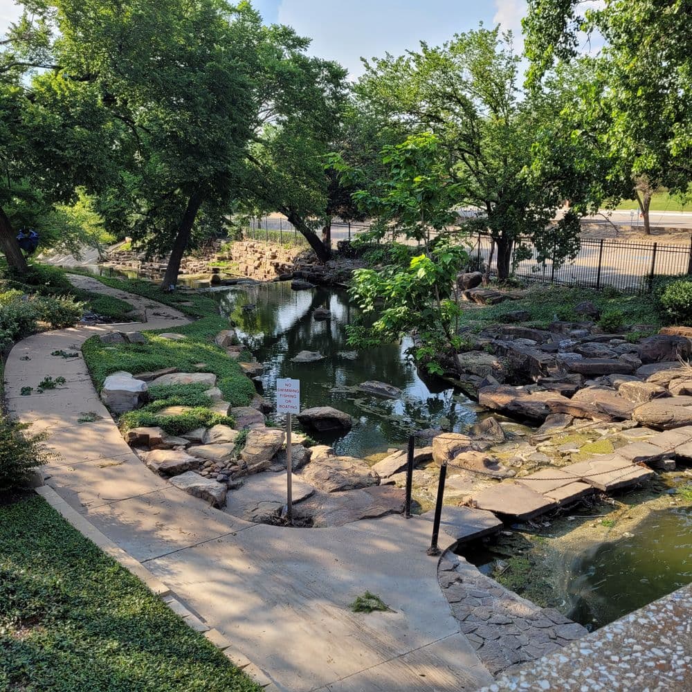 Serene park landscape featuring a winding stream surrounded by lush greenery and rocks.